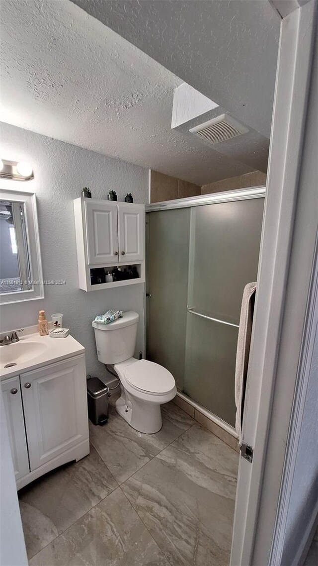 bathroom featuring a textured ceiling, vanity, toilet, and walk in shower