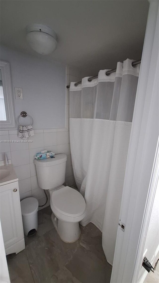 bathroom with vanity, toilet, tile walls, and walk in shower