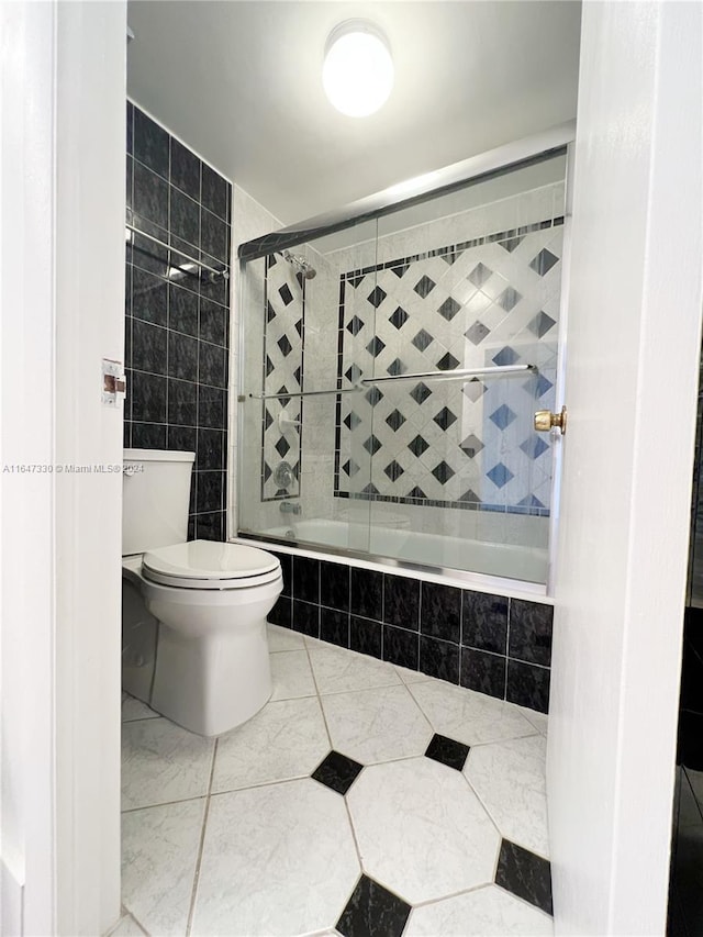 bathroom with tile walls, toilet, and bath / shower combo with glass door