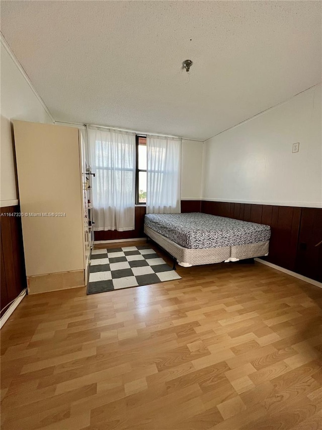 unfurnished bedroom with a textured ceiling, light hardwood / wood-style flooring, and wood walls