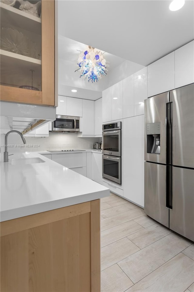 kitchen featuring white cabinetry, tasteful backsplash, an inviting chandelier, sink, and appliances with stainless steel finishes