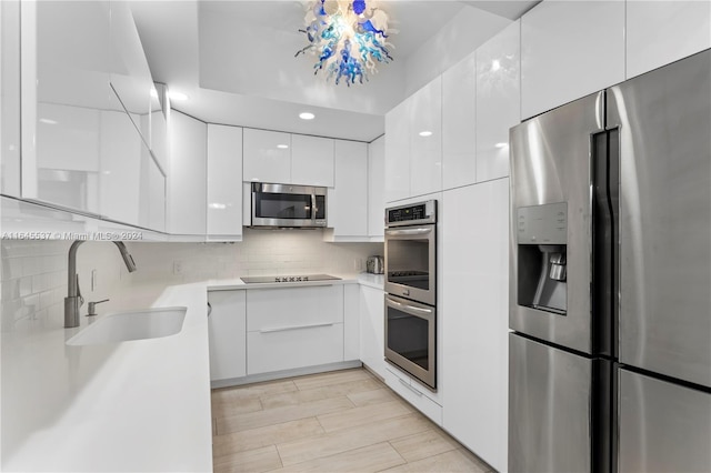 kitchen featuring an inviting chandelier, stainless steel appliances, white cabinetry, sink, and tasteful backsplash