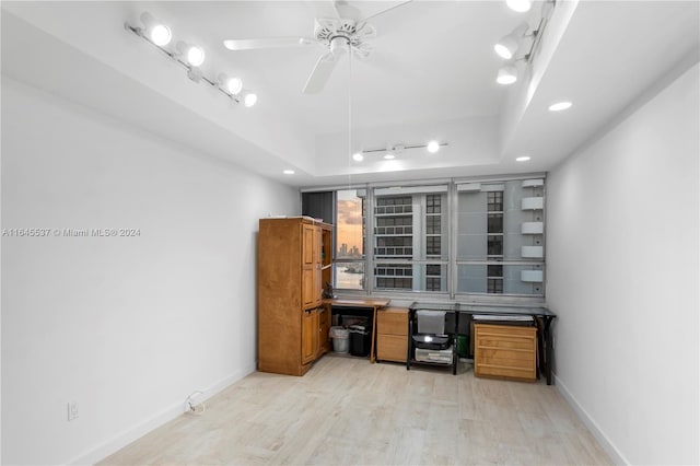 office area with a raised ceiling, light hardwood / wood-style flooring, rail lighting, and ceiling fan