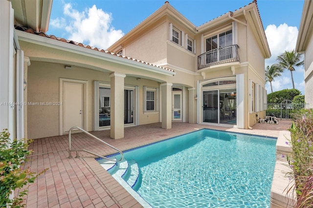 rear view of house with a balcony, a patio area, and a fenced in pool