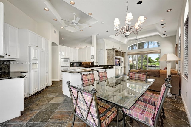 dining room with a raised ceiling, sink, and ceiling fan with notable chandelier