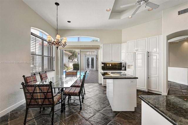 kitchen featuring a high ceiling, ceiling fan with notable chandelier, decorative light fixtures, a kitchen island, and white cabinets