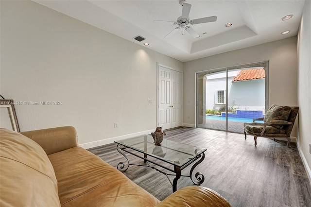 living room with ceiling fan, a raised ceiling, and wood-type flooring