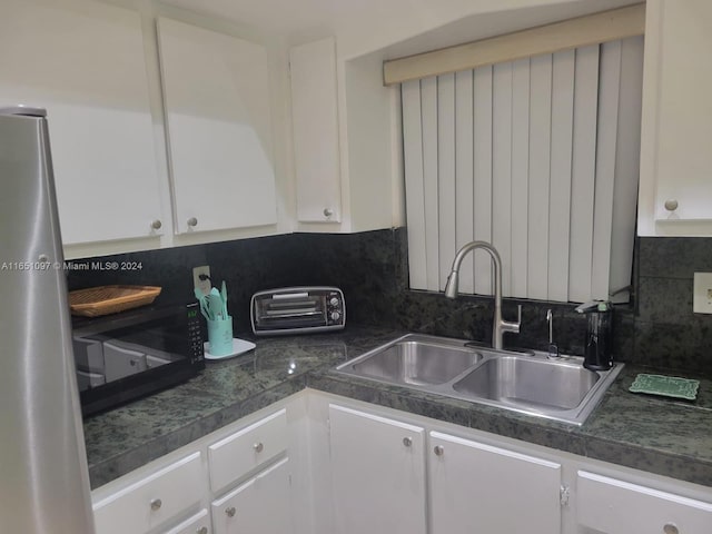 kitchen with stainless steel fridge, white cabinetry, backsplash, and sink