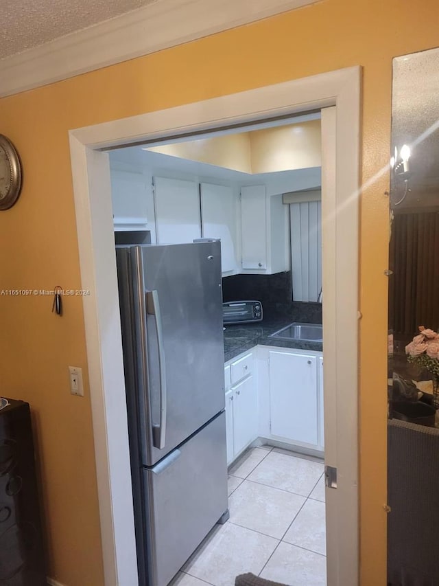 kitchen featuring a textured ceiling, stainless steel fridge, light tile patterned floors, sink, and white cabinetry