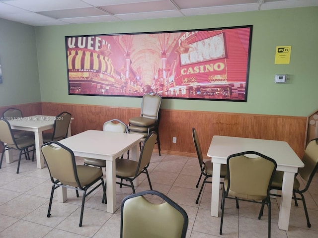 tiled dining space with a paneled ceiling and wooden walls