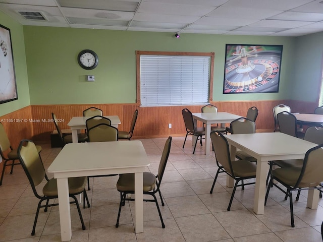 tiled dining space with a paneled ceiling and wooden walls