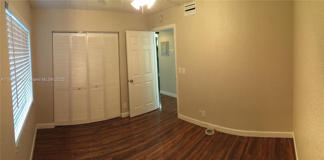 unfurnished bedroom featuring baseboards, visible vents, dark wood finished floors, a textured wall, and a closet
