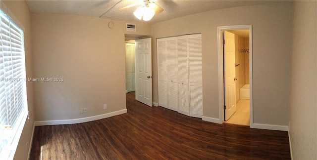 unfurnished bedroom featuring baseboards, visible vents, ensuite bath, dark wood-type flooring, and a closet