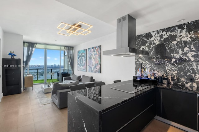 kitchen featuring dark stone counters, wall chimney range hood, a water view, black electric cooktop, and a wall of windows