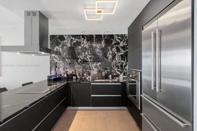 kitchen featuring sink, backsplash, wall chimney range hood, stainless steel appliances, and dark stone counters