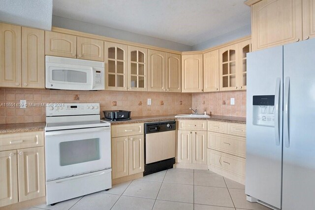 kitchen featuring white appliances, light tile patterned floors, backsplash, sink, and light stone counters