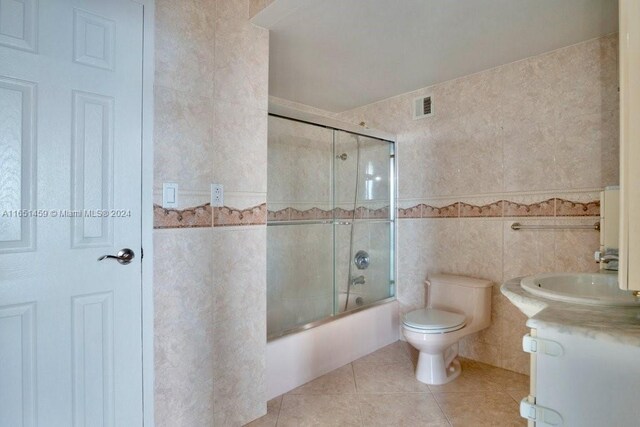 full bathroom featuring vanity, tile patterned flooring, tile walls, toilet, and enclosed tub / shower combo