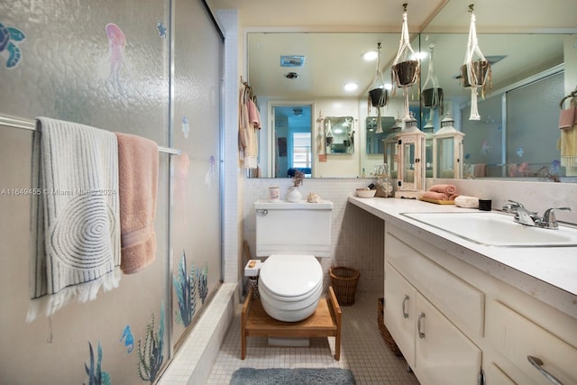 bathroom with a shower with door, vanity, tile patterned flooring, tile walls, and toilet