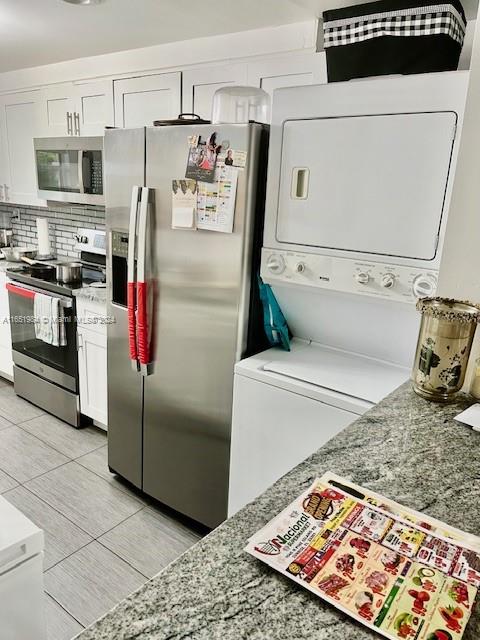 kitchen with stainless steel appliances, white cabinetry, light stone counters, and backsplash