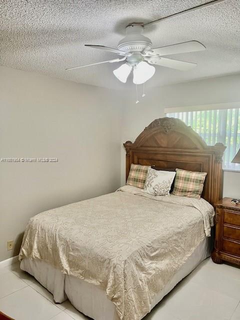 bedroom with ceiling fan, light tile patterned floors, and a textured ceiling