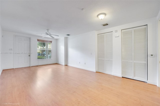 unfurnished bedroom with light wood-type flooring, a textured ceiling, two closets, and ceiling fan