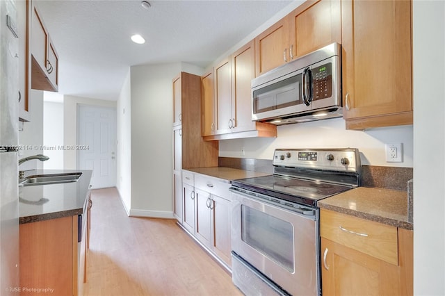 kitchen with dark stone countertops, light wood-type flooring, appliances with stainless steel finishes, sink, and a textured ceiling