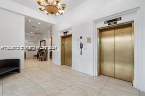 hallway featuring light tile patterned floors, elevator, and a chandelier