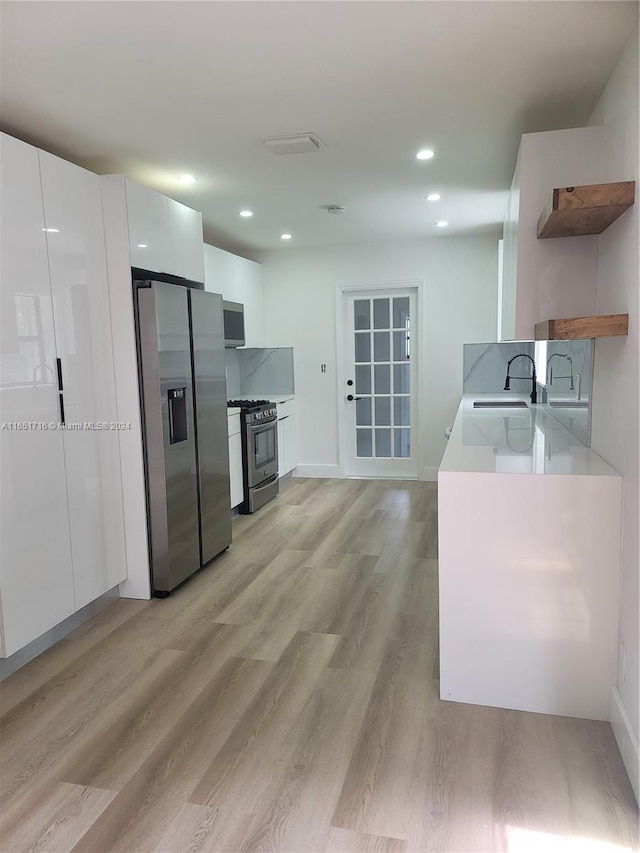 kitchen with stainless steel appliances, sink, light wood-type flooring, and white cabinetry