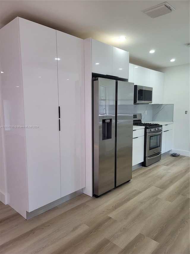 kitchen with stainless steel appliances, backsplash, white cabinets, and light hardwood / wood-style floors