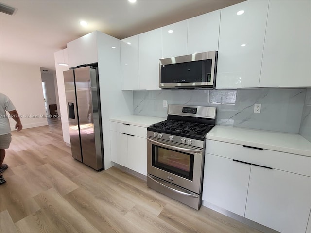 kitchen featuring backsplash, light wood-type flooring, appliances with stainless steel finishes, and white cabinetry