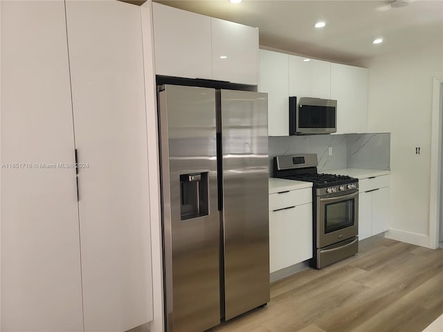 kitchen with light wood-type flooring, appliances with stainless steel finishes, white cabinetry, and decorative backsplash