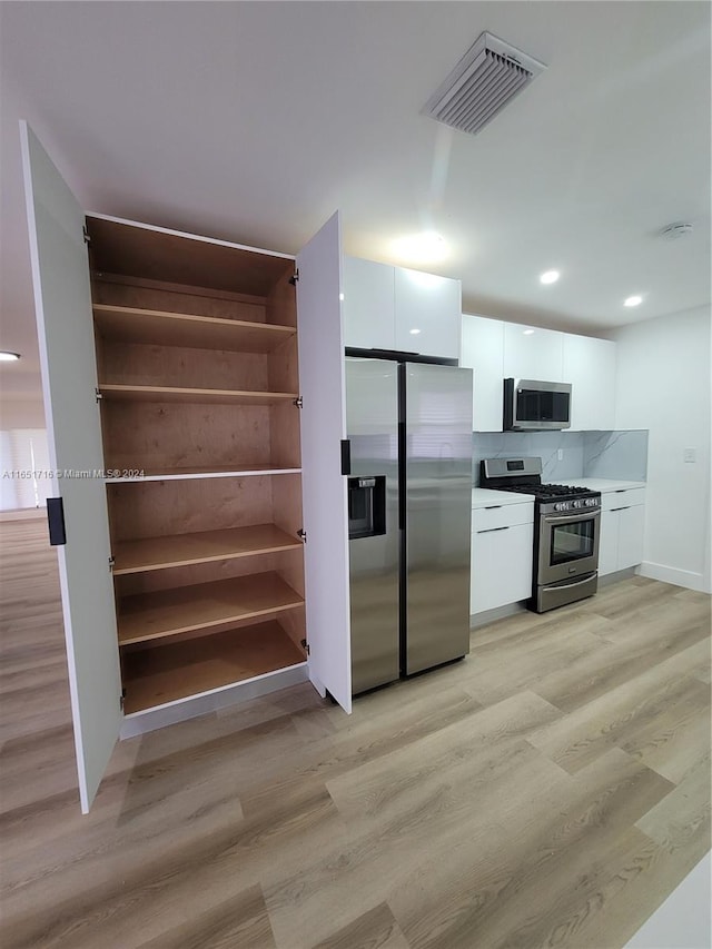 kitchen with light hardwood / wood-style flooring, appliances with stainless steel finishes, white cabinets, and decorative backsplash