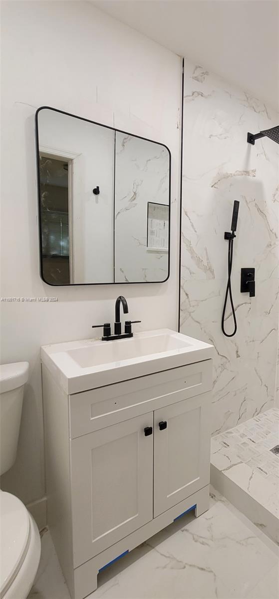 bathroom featuring vanity, toilet, and a tile shower