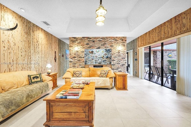 living room featuring a tray ceiling, wooden walls, a textured ceiling, and a brick fireplace