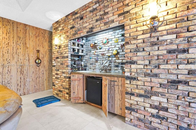 bar with a textured ceiling, brick wall, black refrigerator, wooden walls, and light tile patterned flooring