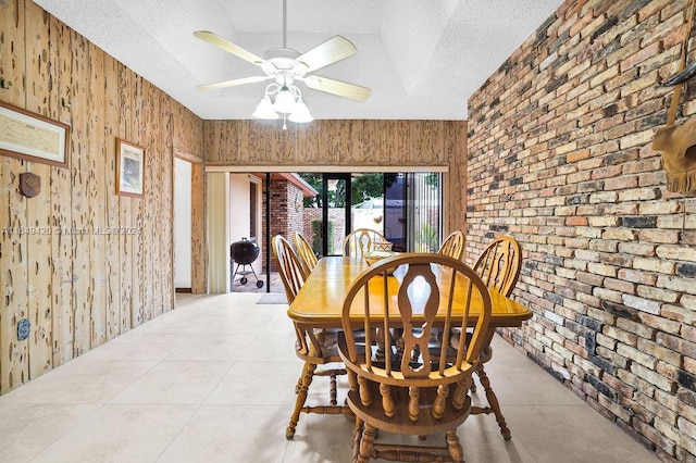 dining area featuring a textured ceiling, brick wall, ceiling fan, and wooden walls