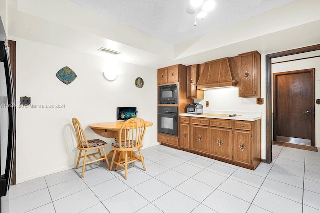 kitchen featuring black appliances, custom exhaust hood, light tile patterned flooring, and a textured ceiling