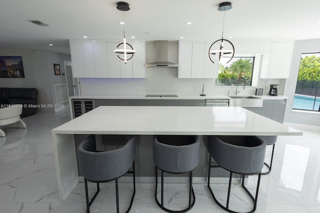 kitchen with white cabinetry, a center island, hanging light fixtures, and wall chimney range hood