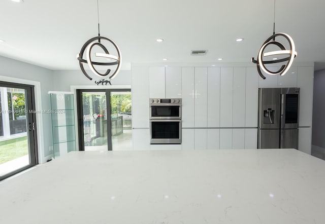 kitchen with light stone counters, decorative light fixtures, appliances with stainless steel finishes, and a wealth of natural light