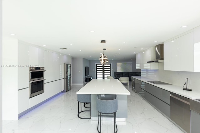 kitchen with white cabinets, pendant lighting, stainless steel appliances, a center island, and wall chimney range hood