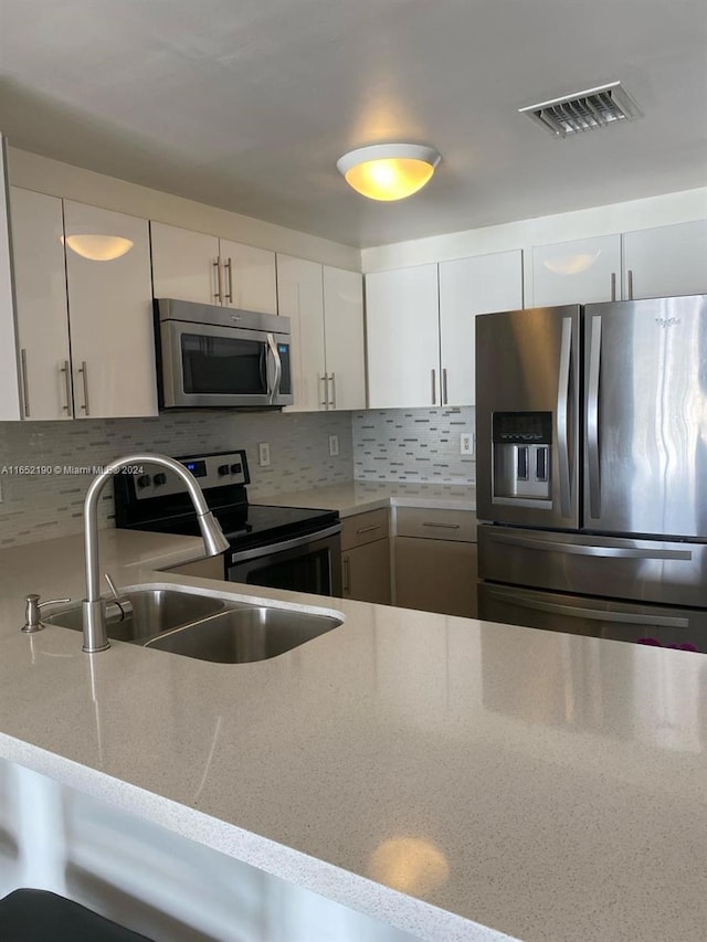 kitchen with light stone countertops, appliances with stainless steel finishes, tasteful backsplash, sink, and white cabinets