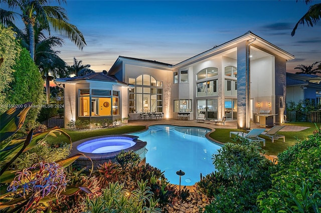 pool at dusk with an in ground hot tub and a patio