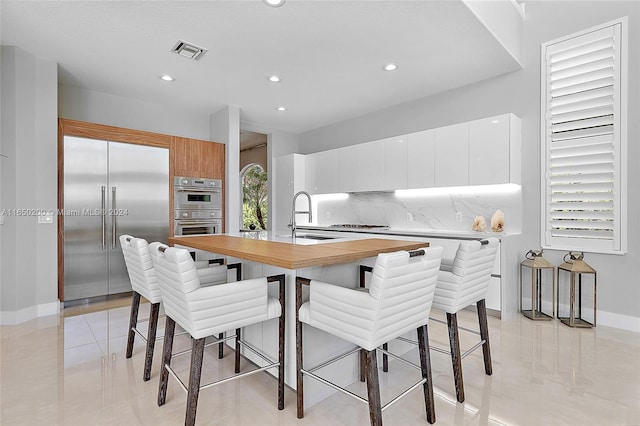 kitchen featuring sink, an island with sink, backsplash, white cabinetry, and stainless steel appliances