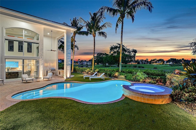 pool at dusk featuring an in ground hot tub, a patio, and a lawn