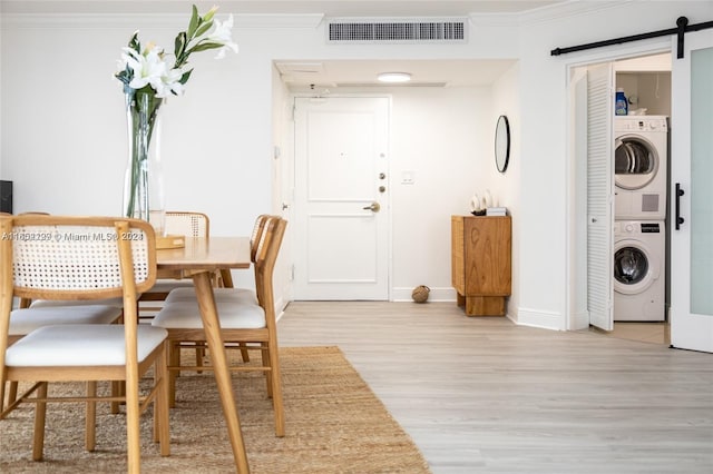 dining space featuring crown molding, light hardwood / wood-style flooring, a barn door, and stacked washing maching and dryer