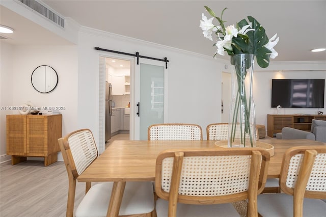 dining space featuring crown molding, light wood finished floors, visible vents, and a barn door