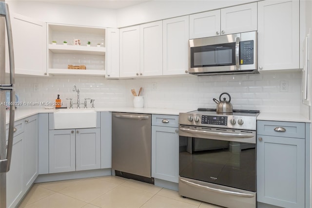 kitchen featuring stainless steel appliances, a sink, open shelves, light countertops, and tasteful backsplash