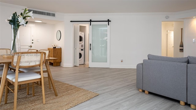 living room featuring stacked washer and dryer, light wood finished floors, crown molding, and a barn door