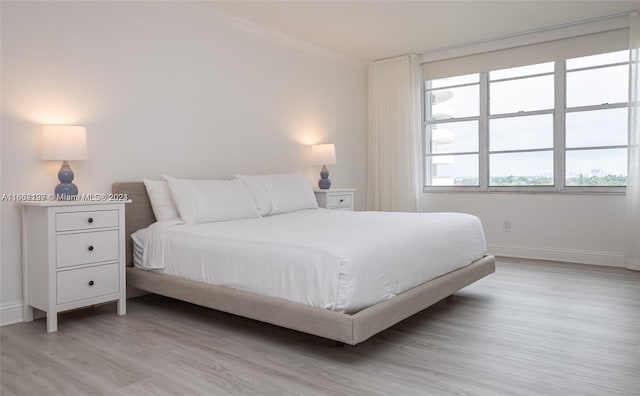 bedroom featuring crown molding, light wood-style flooring, and baseboards