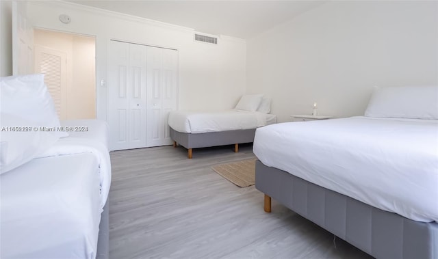bedroom featuring a closet, visible vents, wood finished floors, and crown molding